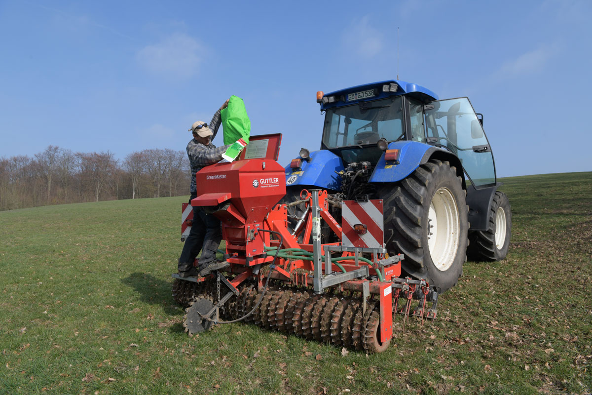 Ein Landwirt füllt auf dem Feld Saatgut in den Behälter. Klick führt zu Großansicht im neuen Fenster. 