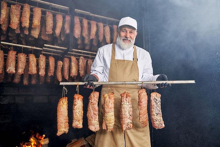 Mann steht in einer Räucherkammer mit Fleisch. Klick führt zu Großansicht im neuen Fenster.