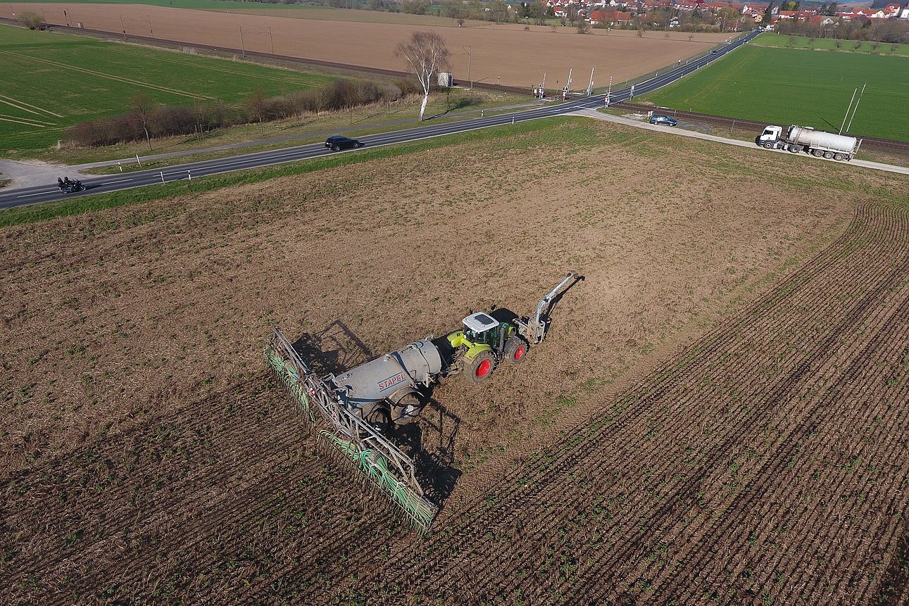 Schlepper mit angehängtem großen Güllefass bringt Wirtschaftsdünger auf einem Feld aus. Am Feldrand steht ein Tanklaster zum Nachfüllen. Klick führt zu Großansicht in neuem Fenster.