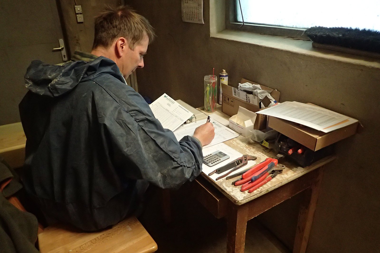 Ein Mann sitzt an einem Schreibtisch und übertragt Daten handschriftlich in eine Tabelle. Klick führt zu Großansicht in neuem Fenster.