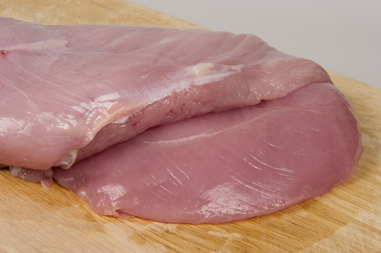 Auf einem Holzbrett liegt ein Stück Putenbrust. Klick führt zu Großansicht im neuen Fenster.  