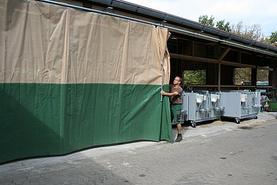 Ein Mann zieht ein Windschutznetz am Außenstall zu. Klick führt zu Großansicht in neuem Fenster.