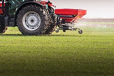 Traktor mit Mineraldüngerstreuer im Einsatz auf Grünland. Klick führt zu Großansicht im neuen Fenster.