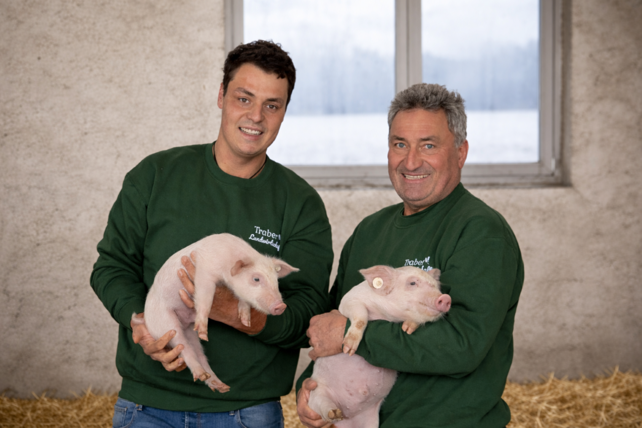 Zwei Männer stehen nebeneinander und halten jeweils zwei größere Ferkel auf dem Arm. Klick führt zu Großansicht im neuen Fenster. 