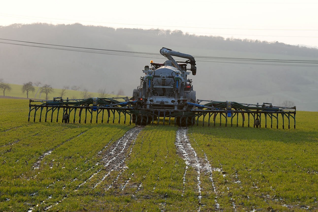 Traktor mit Güllefass und Schleppschläuchen von hinten auf einem Feld. Klick führt zu Großansicht in neuem Fenster.